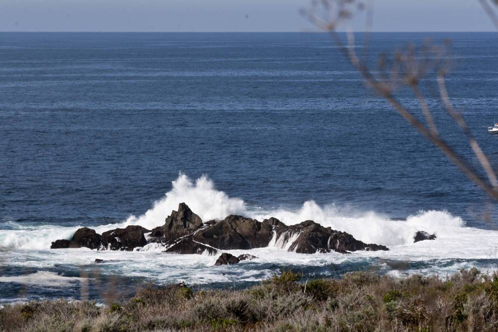 Waves crash white against a cluster of dark rocks just offshore.