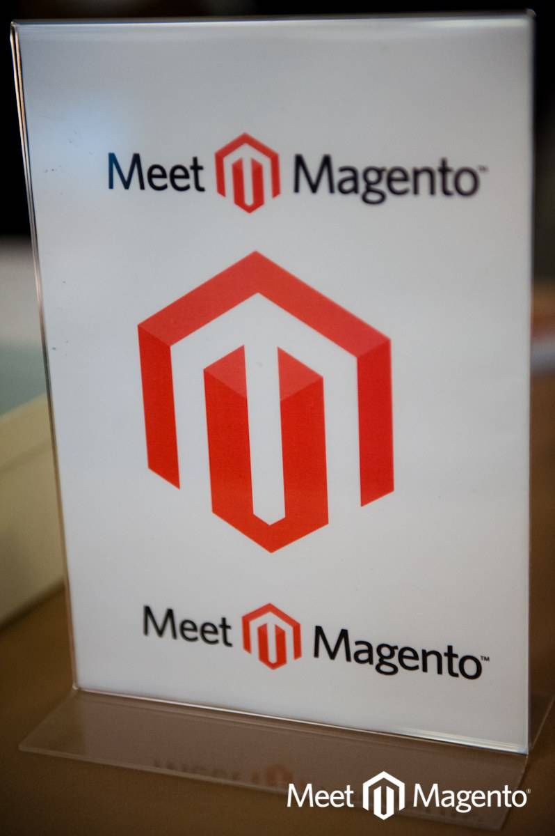 A 'Meet Magento' sign with the red Magento logo standing on a table.