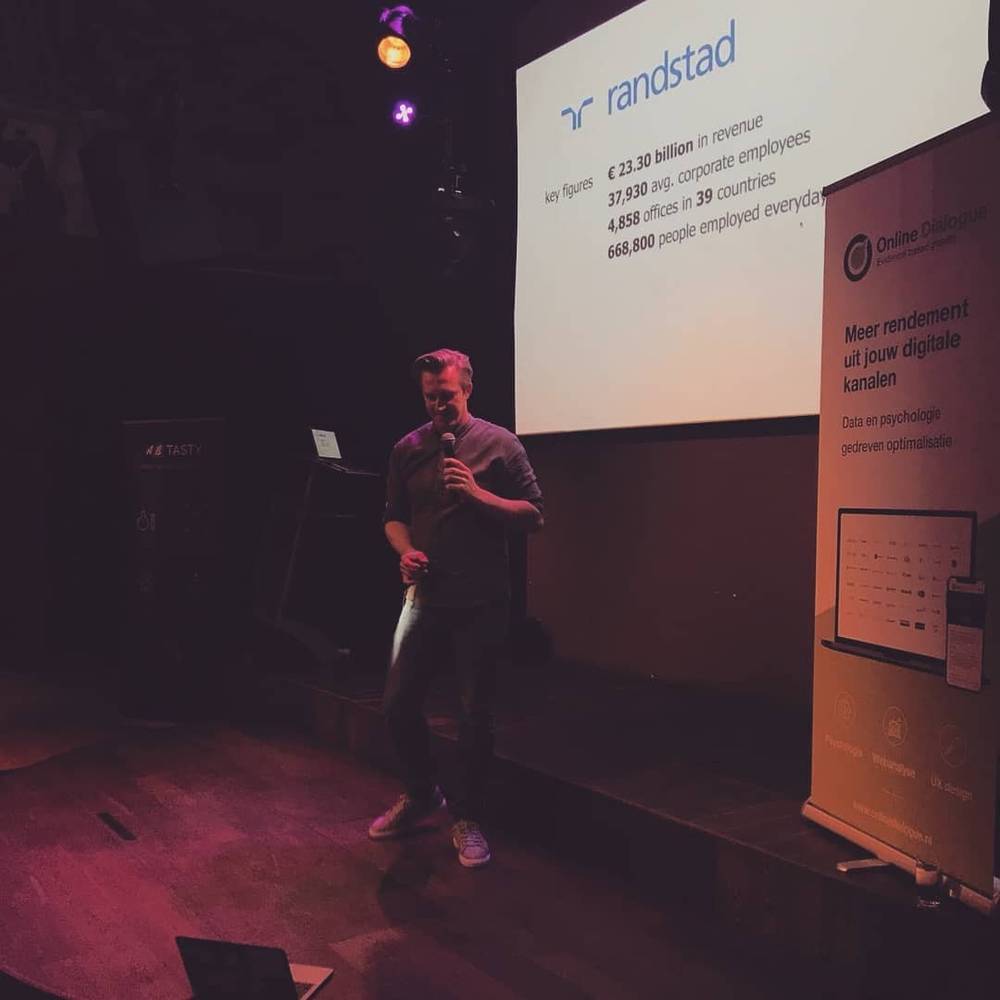 A man presenting on stage in front of a Randstad slide showing company key figures.