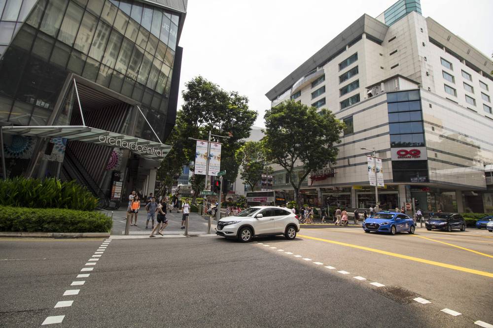 A street corner is lined with modern shopping mall facades.