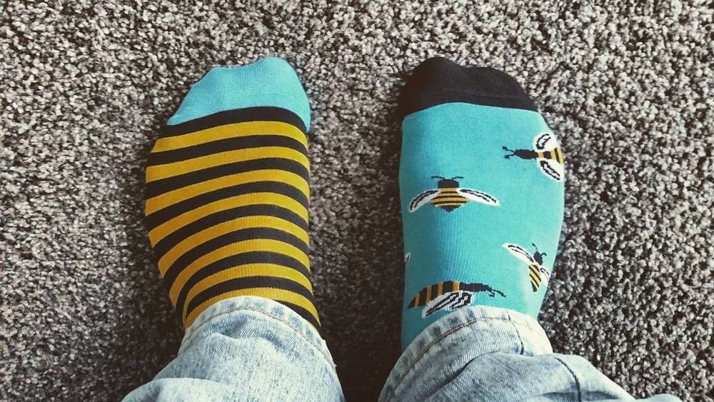 Two feet showing mismatched striped and bee-patterned socks on a carpet.