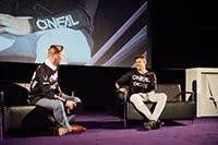 Two people seated on a stage, partially visible, in conversation.