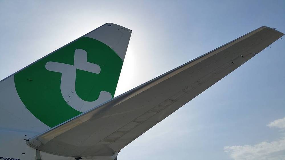 The green-tipped wingtip of a Transavia plane against a bright sky.