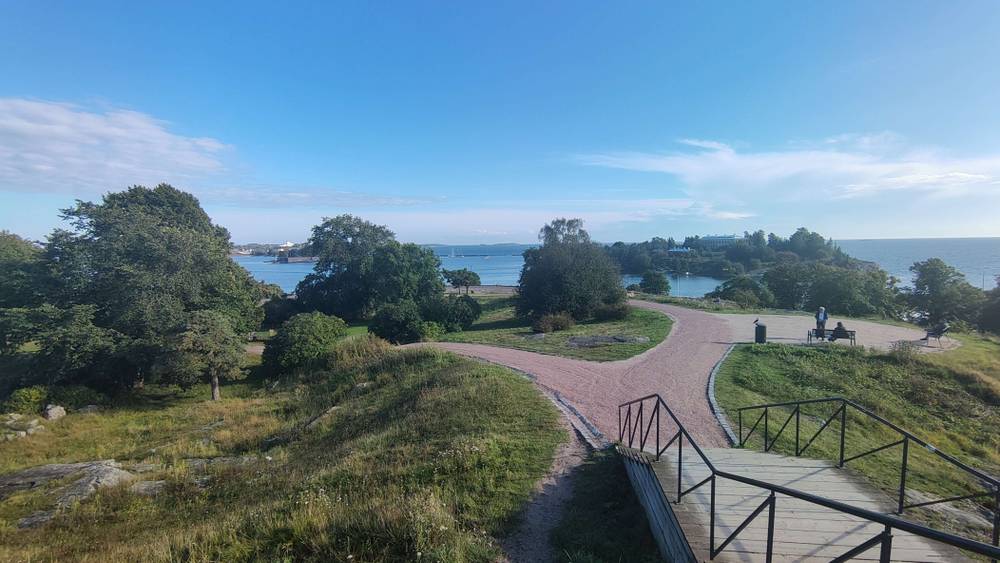 A paved path curves through parkland overlooking the sea.
