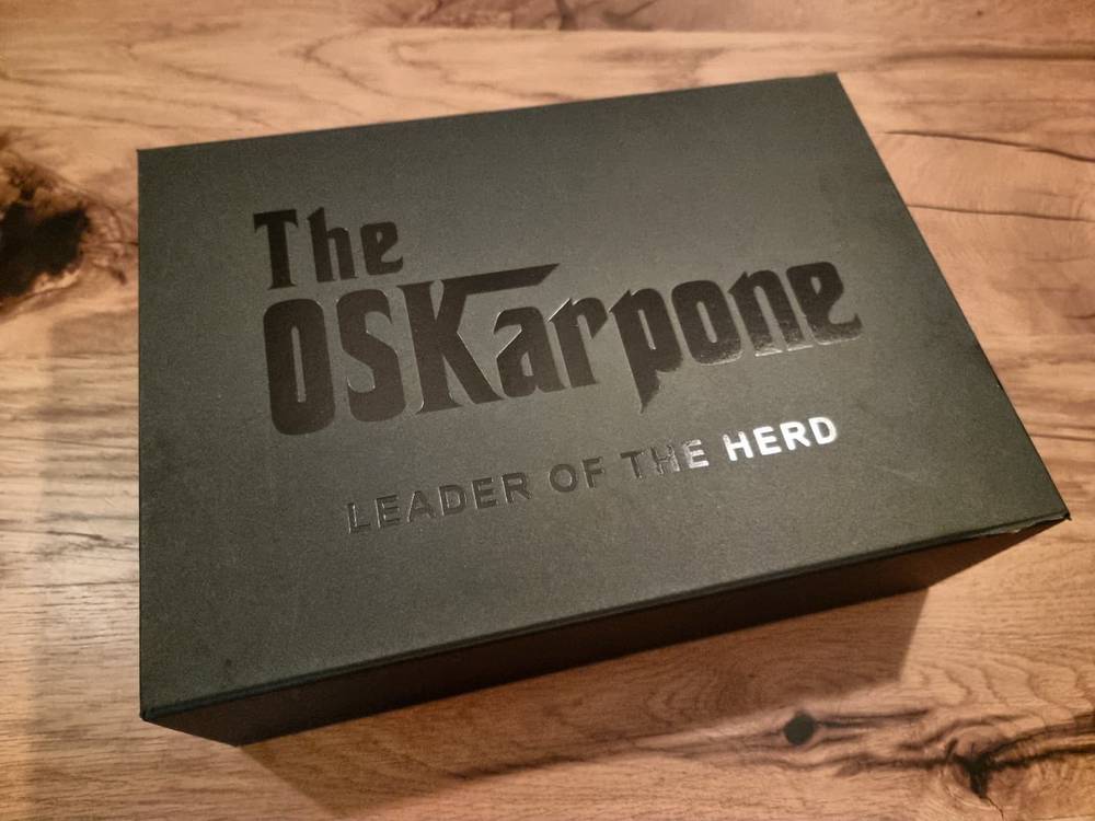 A dark gift box on a wooden floor printed with the text "The OSKarpone – Leader of the Herd."