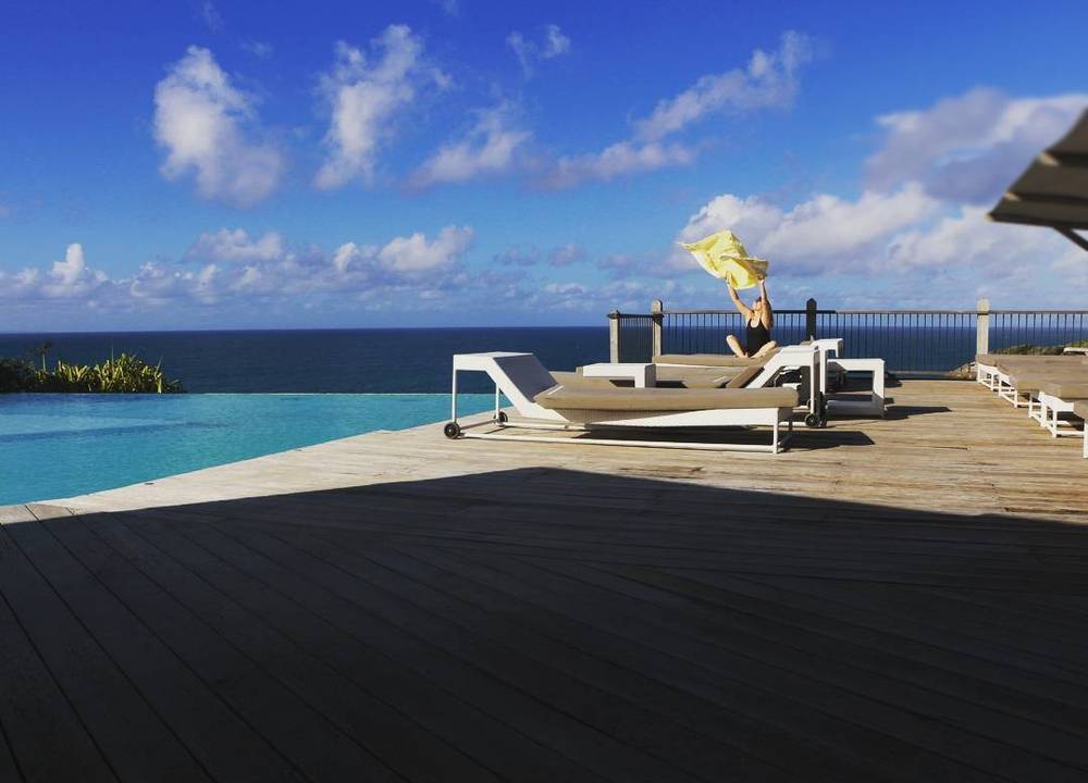 A woman jumping near a swimming pool overlooking the ocean.