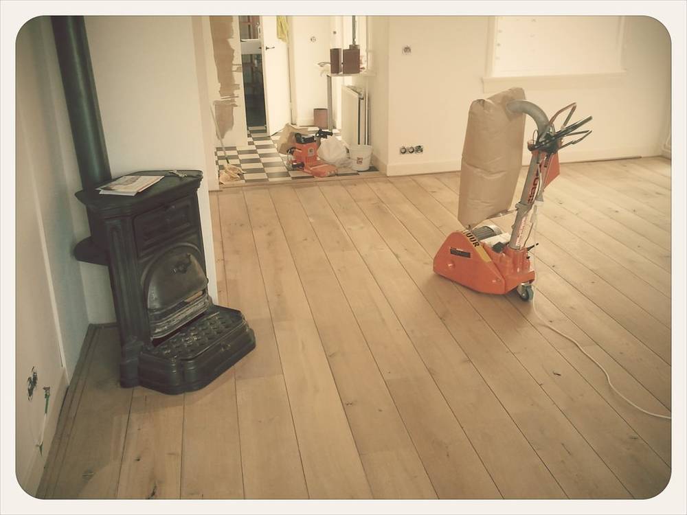 A wood floor sander stands in a room mid-renovation next to an old stove.