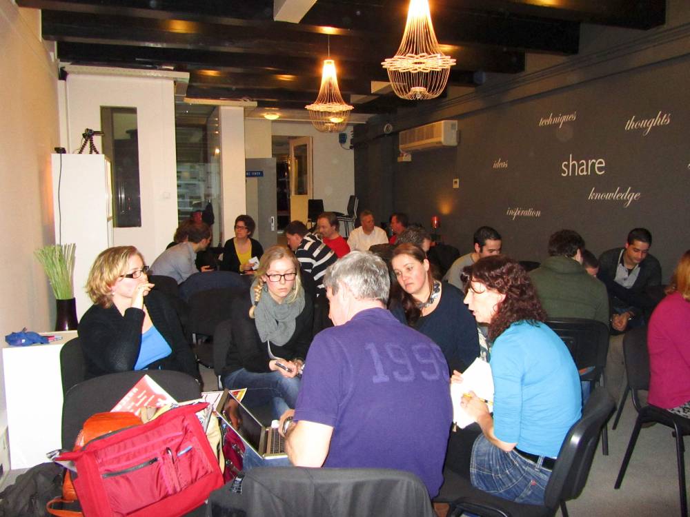 Workshop attendees sit in small discussion groups in a room decorated with wall text.