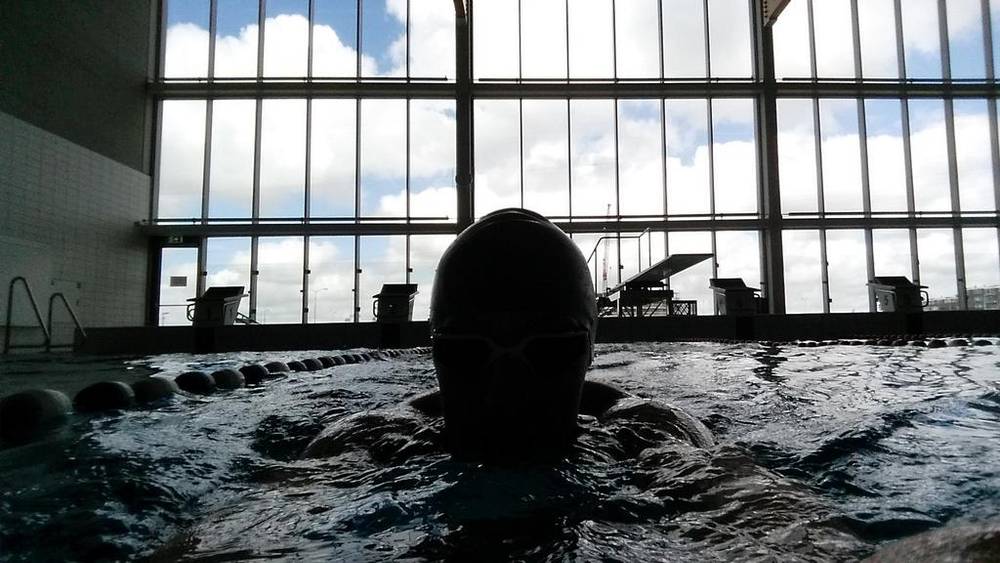 A backlit silhouette of a swimmer's head emerging from pool water.