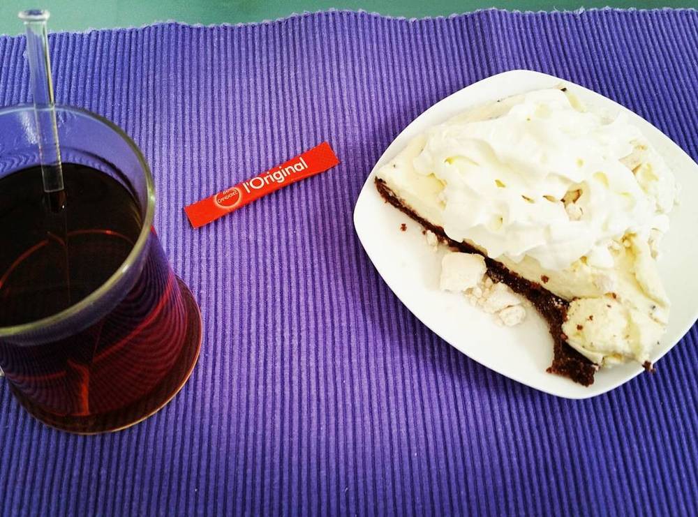 A glass of mulled wine, a sweetener packet, and a slice of cake with whipped cream on a purple mat.