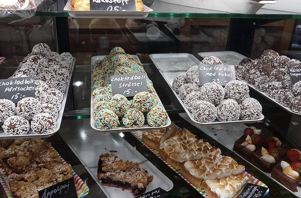 A bakery display case filled with Swedish chocolate balls and fruit tarts.
