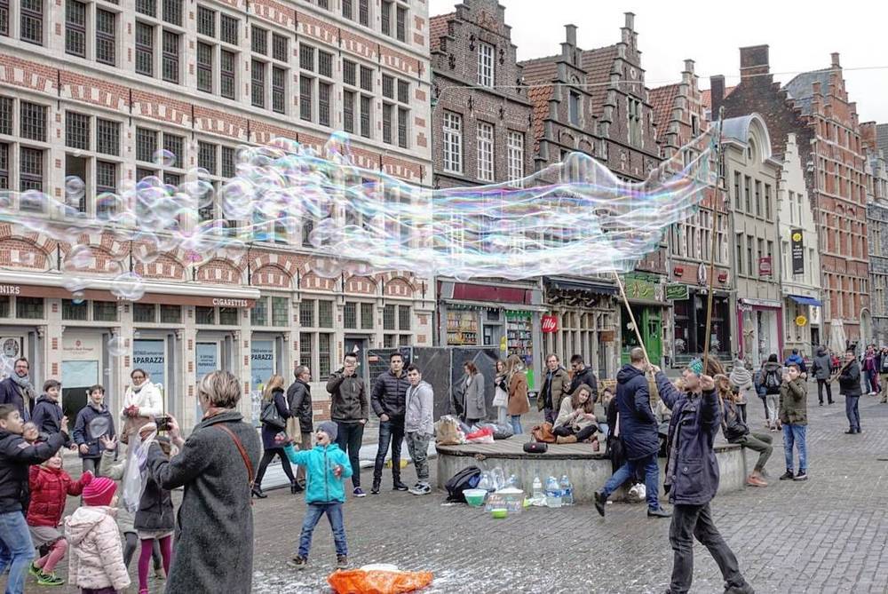 A street performer creating giant soap bubbles for a crowd in a historic square.