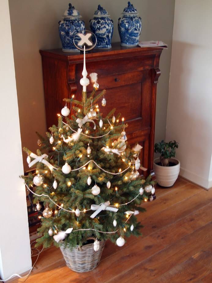 A small decorated Christmas tree topped with an x.commerce ornament sits atop a wooden cabinet.