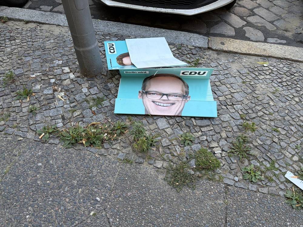 ein cdu wahlkampfplakat liegt leicht gefaltet auf dem boden. das foto des kandidaten wird dadurch verzerrt und witzig