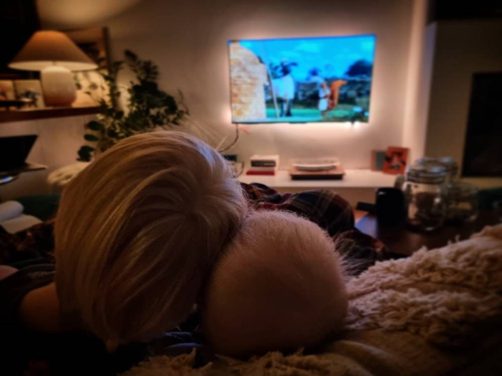 A person resting with their head down on a cushion, a golf match playing on a TV in the background.