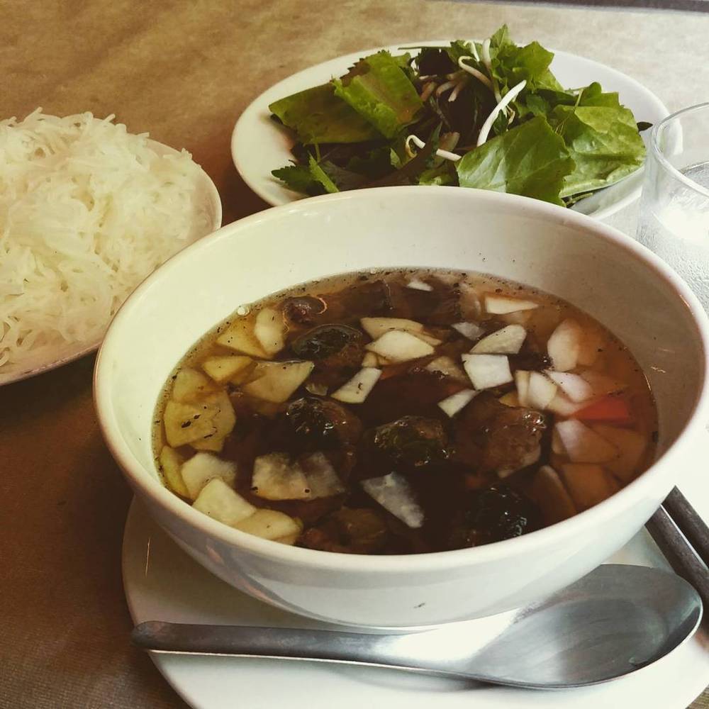 A bowl of dark broth soup with meat and radish, served with a bowl of rice and fresh greens.