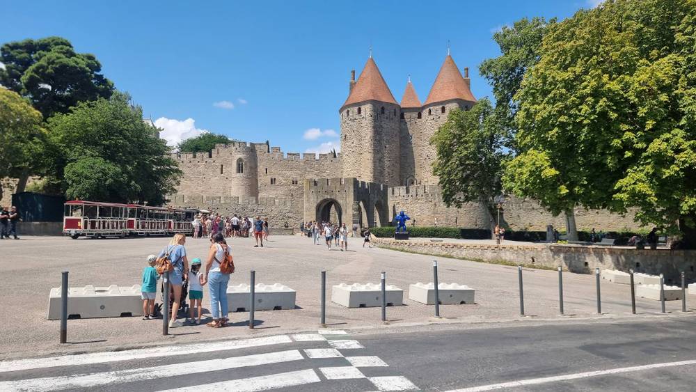 People stand near a medieval walled citadel with stone towers.
