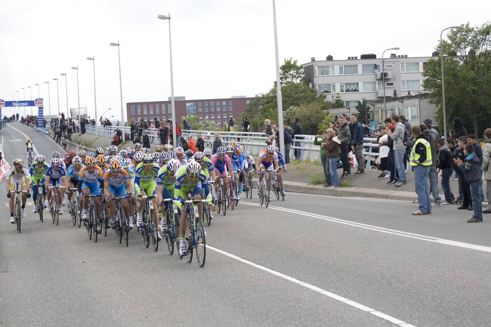 The peloton rides tightly packed across the bridge as spectators line the railings.