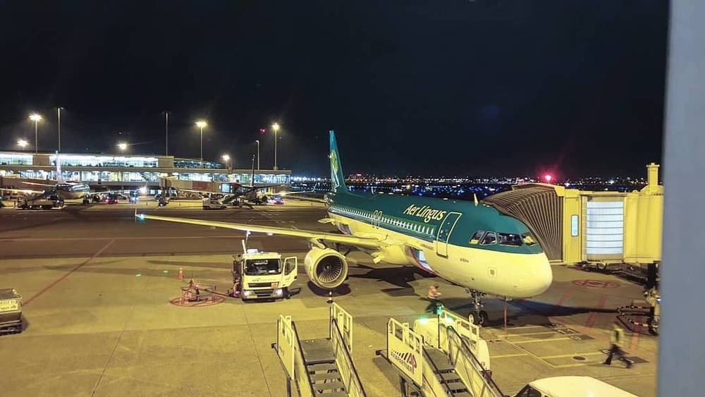 An airplane sits on the tarmac at night with a jet bridge and ground crew nearby.