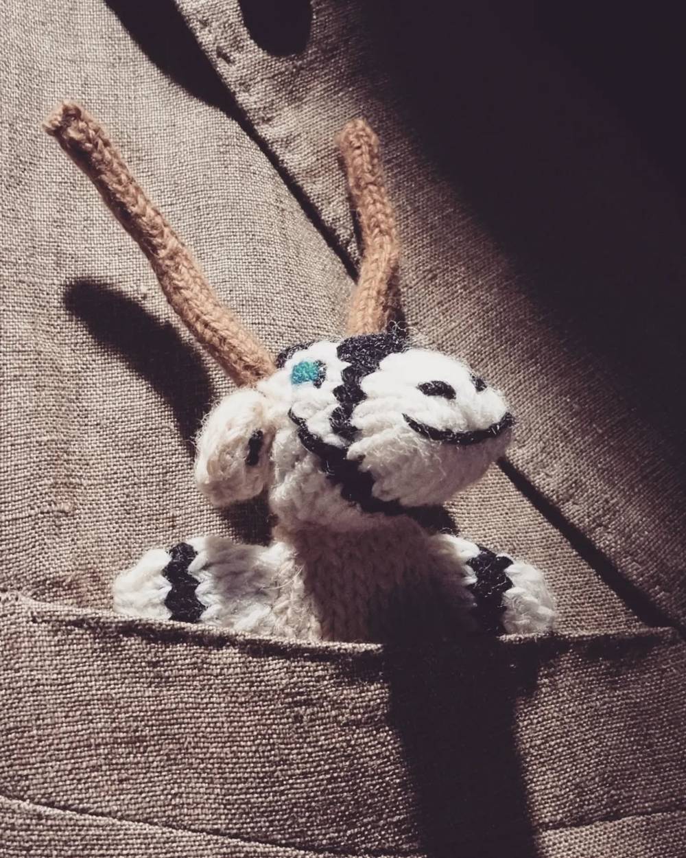A small knitted toy goat figure tucked into a woven fabric pocket.