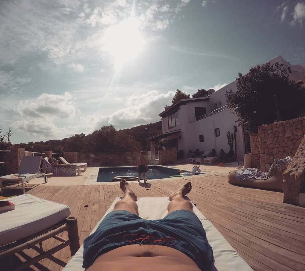 A person relaxing on a lounger by a pool at a villa, feet in the foreground.