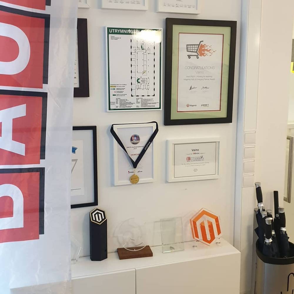 A display shelf holds framed certificates, medals and Magento trophies on an office wall.