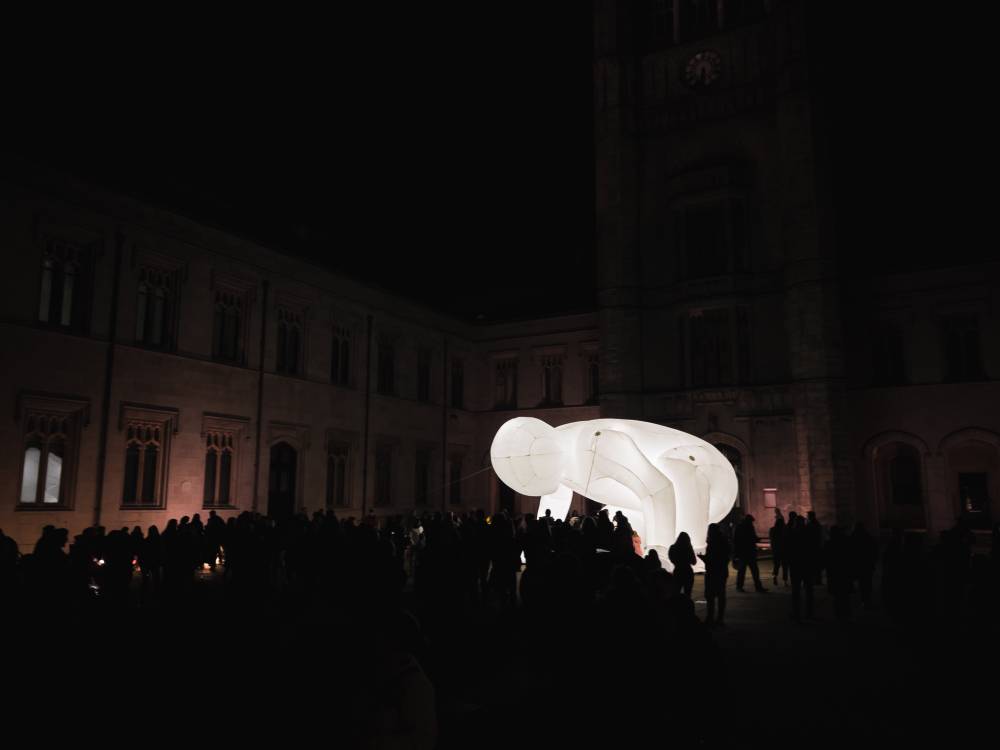 A light installation. A white light character towers over crowd at night. 