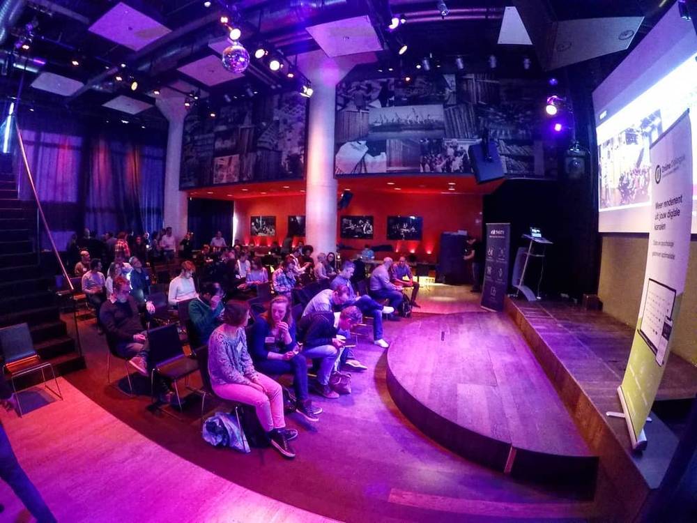 A conference audience seated in a venue lit with purple stage lighting.