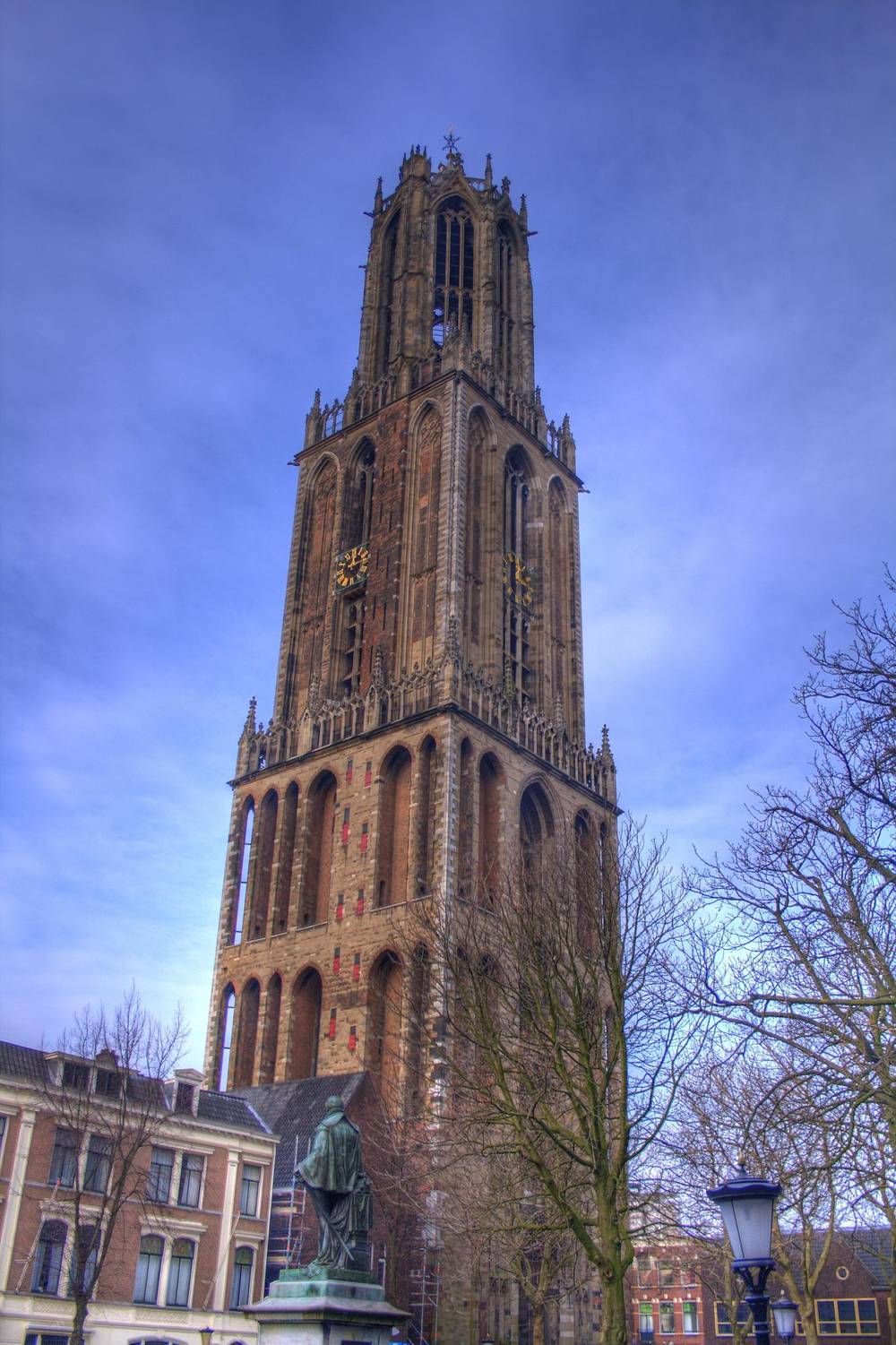The Dom Tower rises above a statue and rooftops under a clear blue sky.
