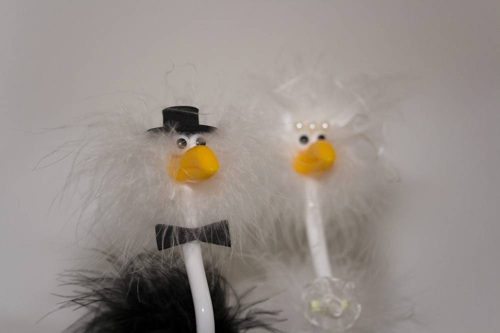 Two feather-and-bead puppet decorations wearing tiny top hats, used as table decor.