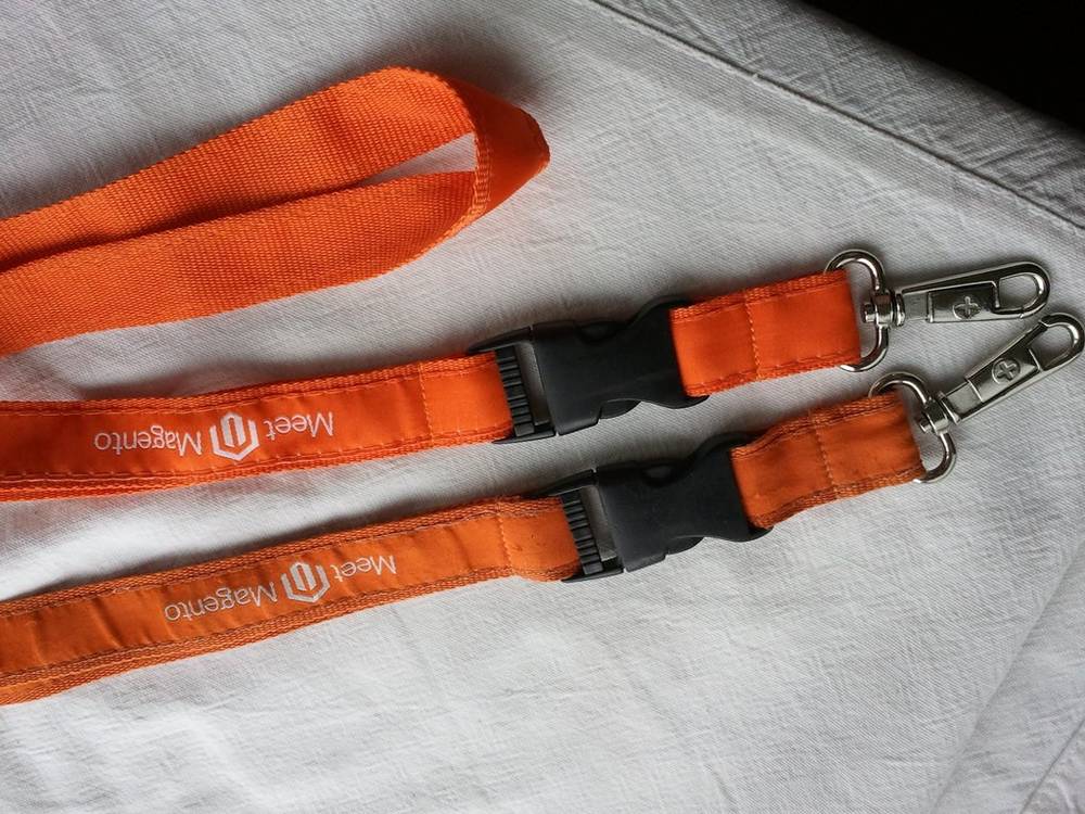 Two orange Meet Magento lanyards lie side by side on a bed.