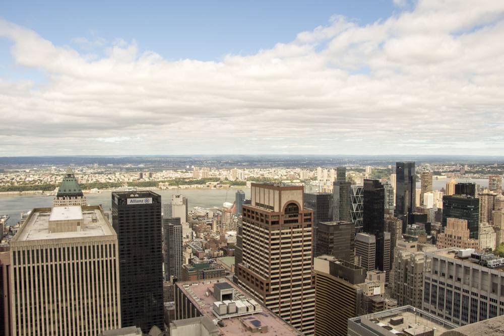 The Hudson River and Manhattan skyline stretch out beneath a cloudy sky from a high viewpoint.