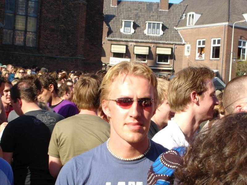 A blond man in sunglasses stands amid a dense street crowd at a liberation day gathering.