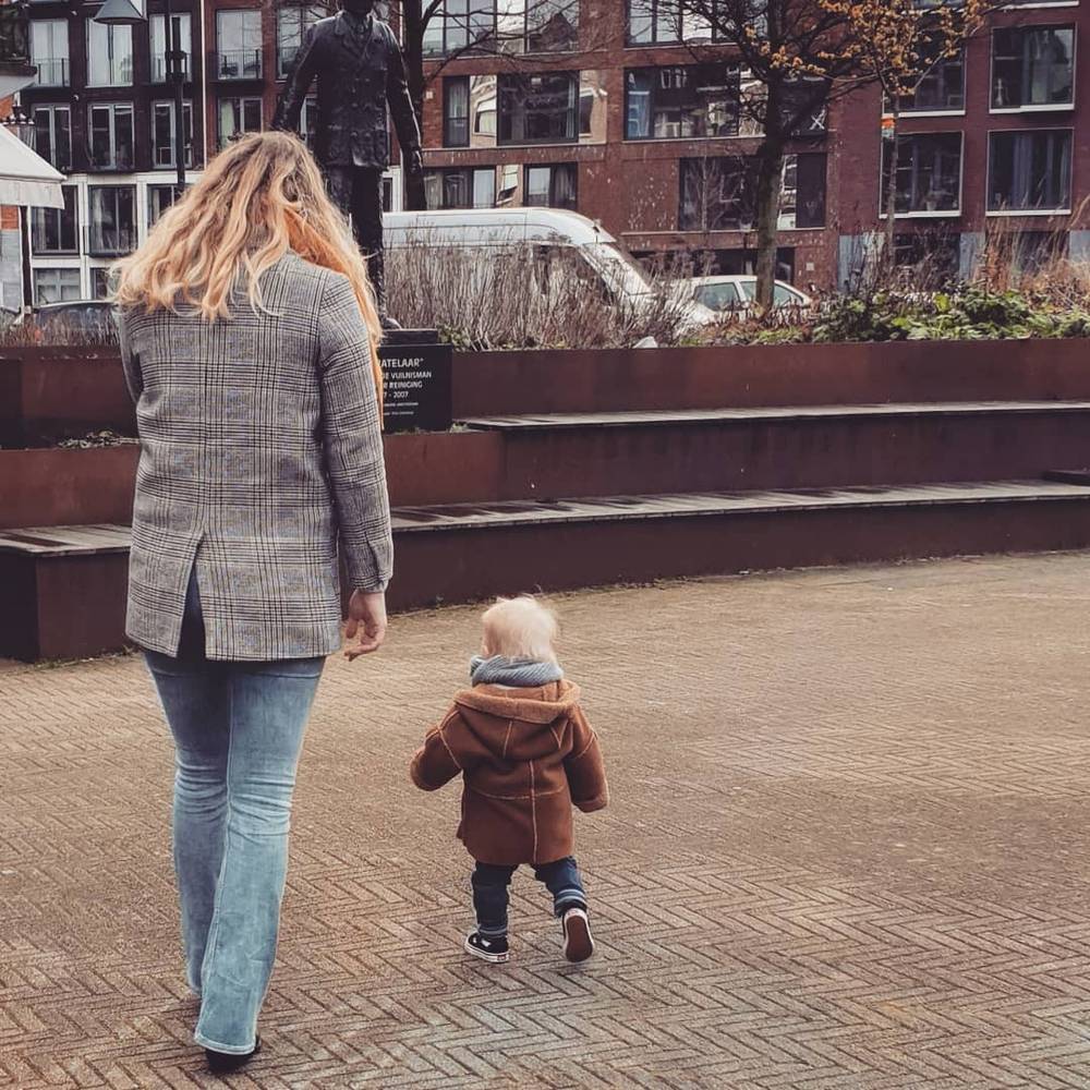 A woman and a toddler walk away down a paved path near a modern building.