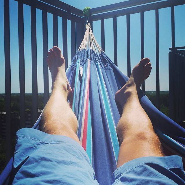 A person's bare legs and feet resting in a striped hammock on a balcony.