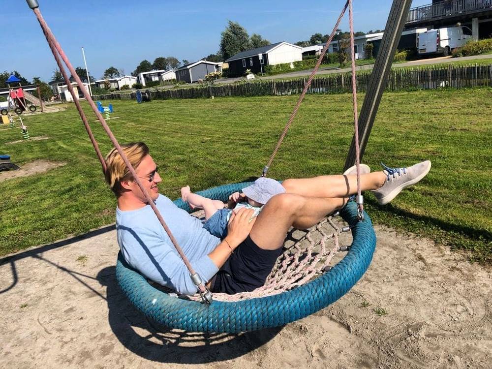 A man reclining in a large round hanging swing chair on a grassy campsite lawn.
