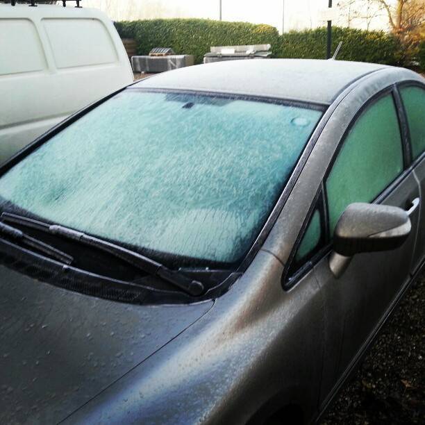 A frosted car windshield and side windows covered in overnight ice.