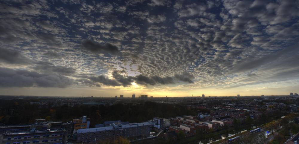A wide panorama of mottled clouds glowing at sunset above Utrecht's rooftops.
