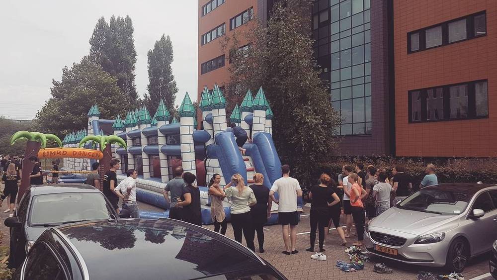 A large inflatable bouncy castle set up outside an office building, with people gathered around.