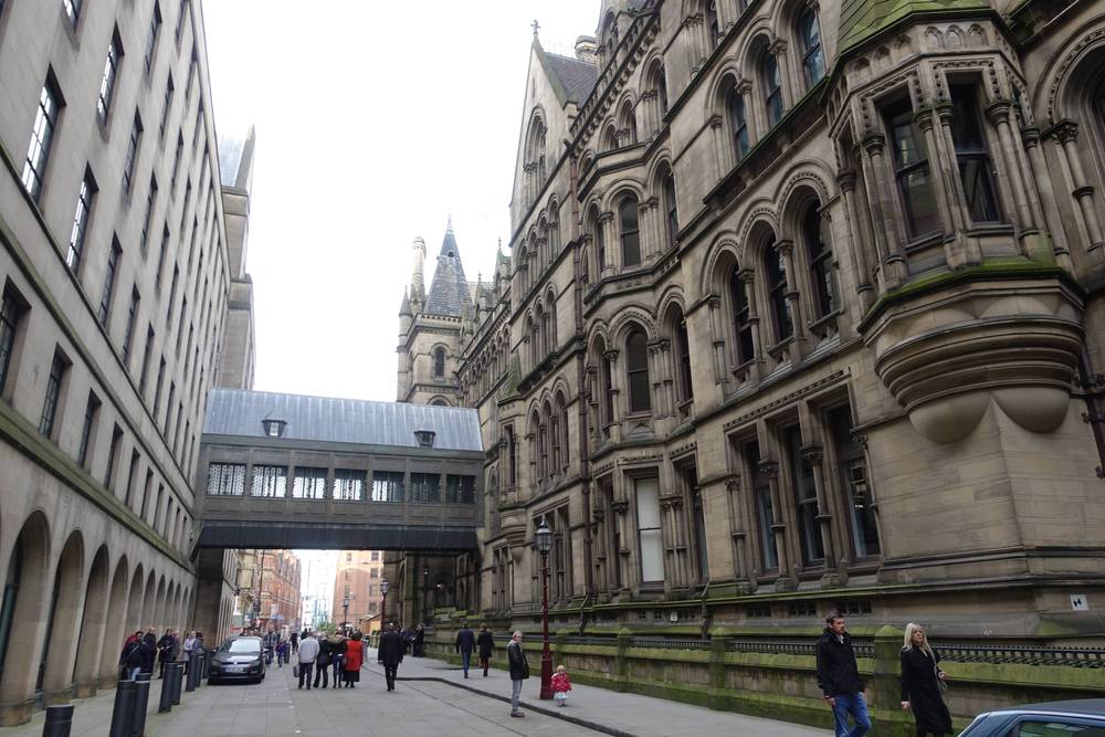 Crowds line a street beside Manchester Town Hall's Gothic facade.