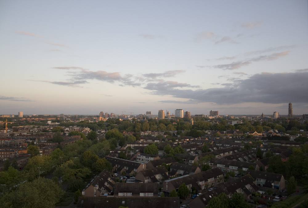 A pale dawn sky with scattered clouds glows over the Utrecht skyline and rooftops.