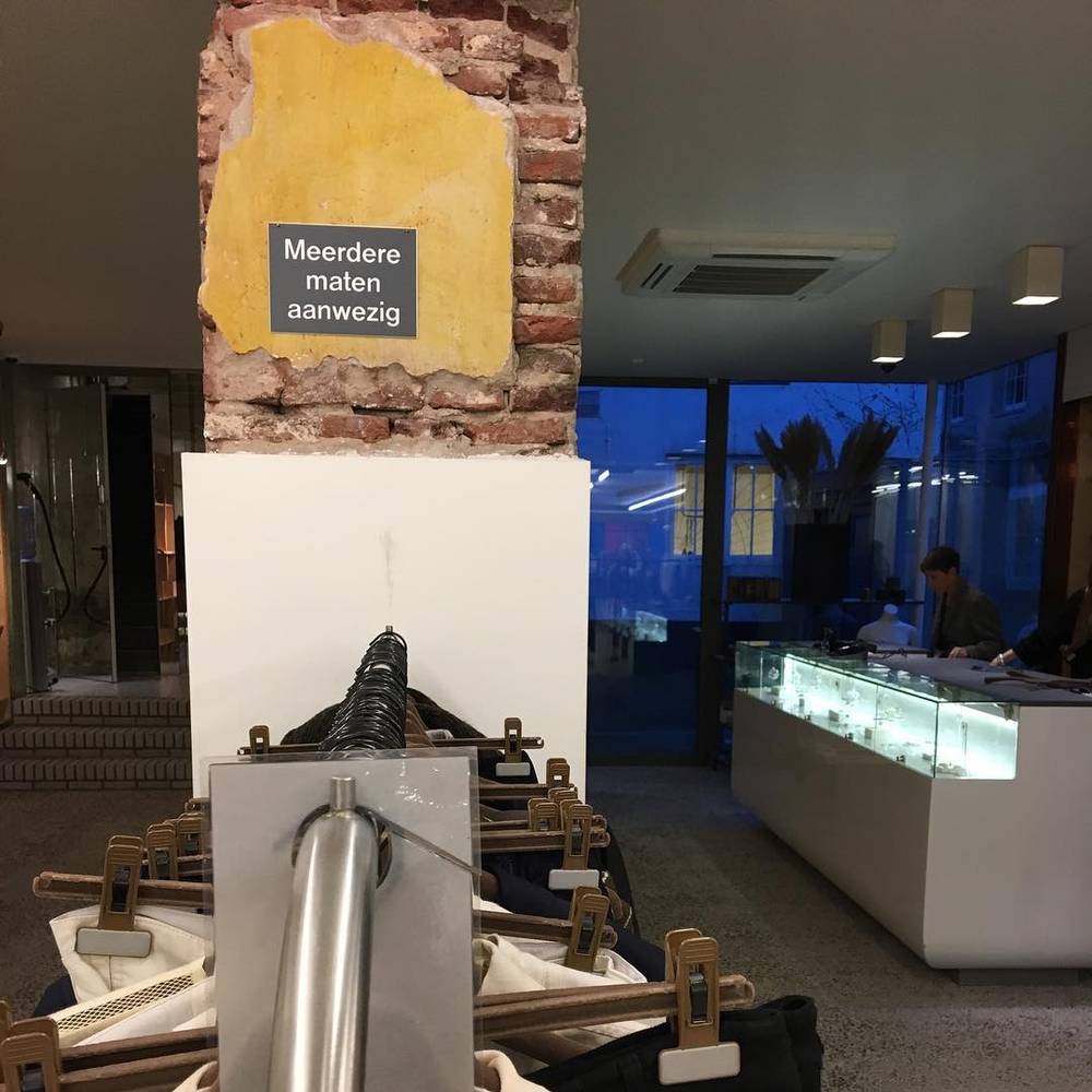 A clothing rack with a sign reading "Meerdere maten aanwezig" (multiple sizes available) in a modern shop.
