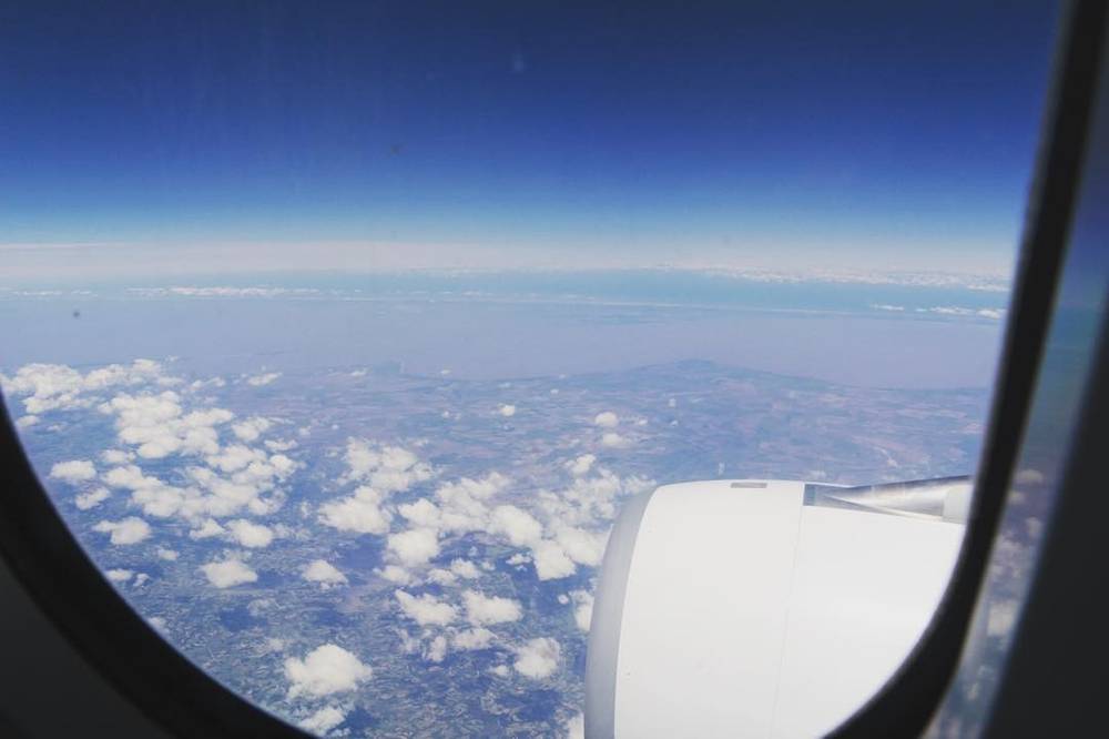 A view from an airplane window looking down over clouds and the curve of the earth.