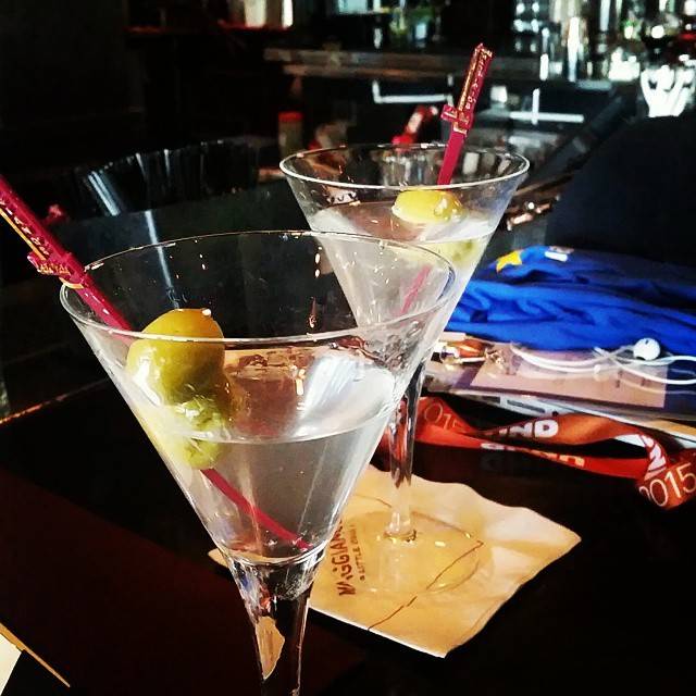Two martini glasses garnished with olives on a bar table.
