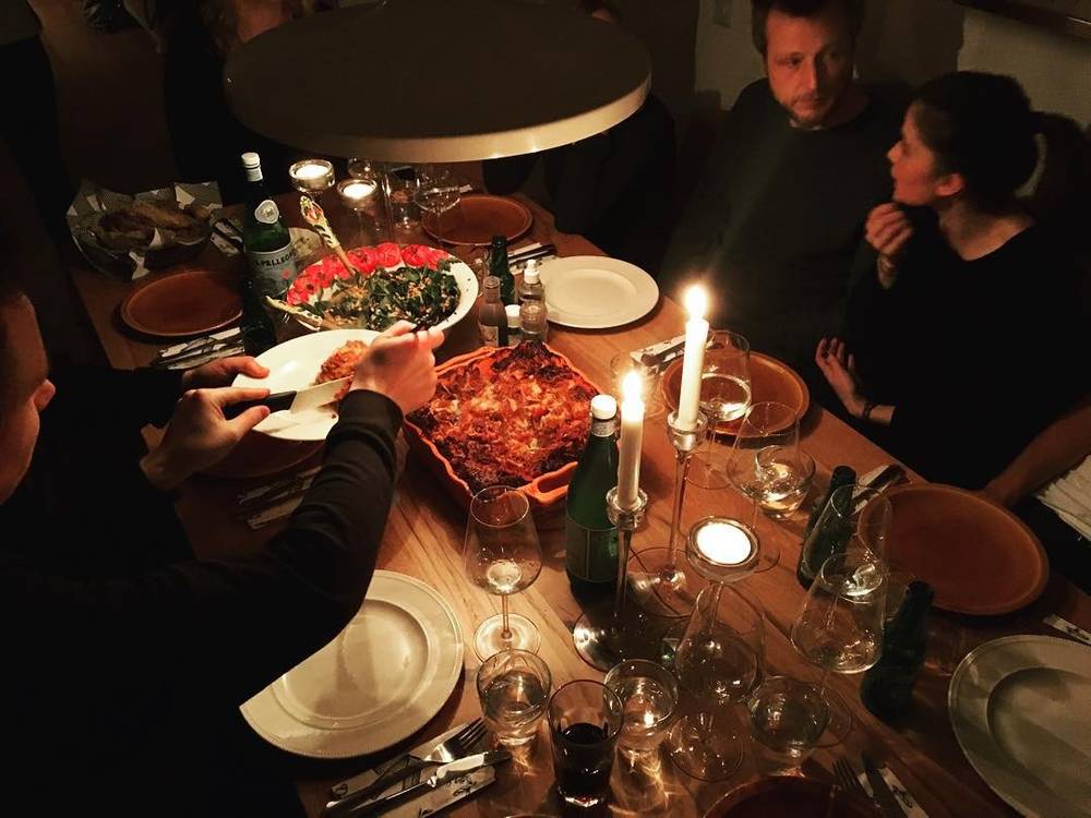 People sharing a meal by candlelight at a long dinner table.