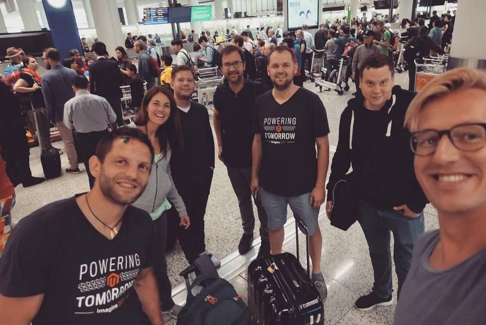 A group of colleagues posing at the airport with luggage, wearing matching "Powering Tomorrow" t-shirts.