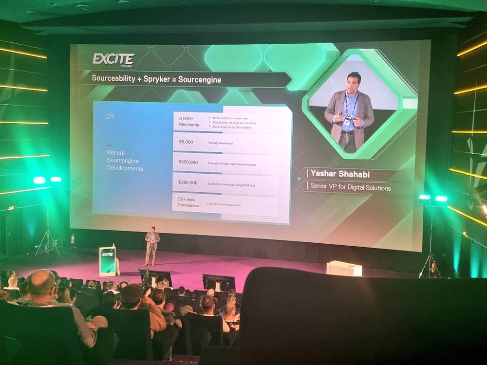 A speaker presenting a slide about 'Sourceability + Spryker = Sourcengine' at the Excite conference.