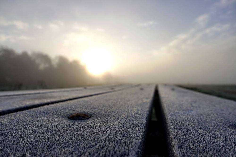 Frost-covered road markings with the sun rising over a misty field.