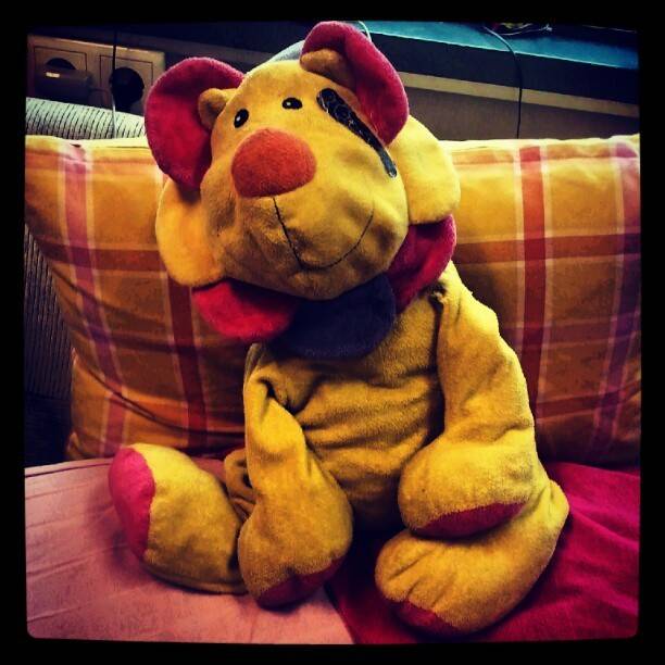 A yellow plush toy dog with red ears propped against pillows on a sofa.