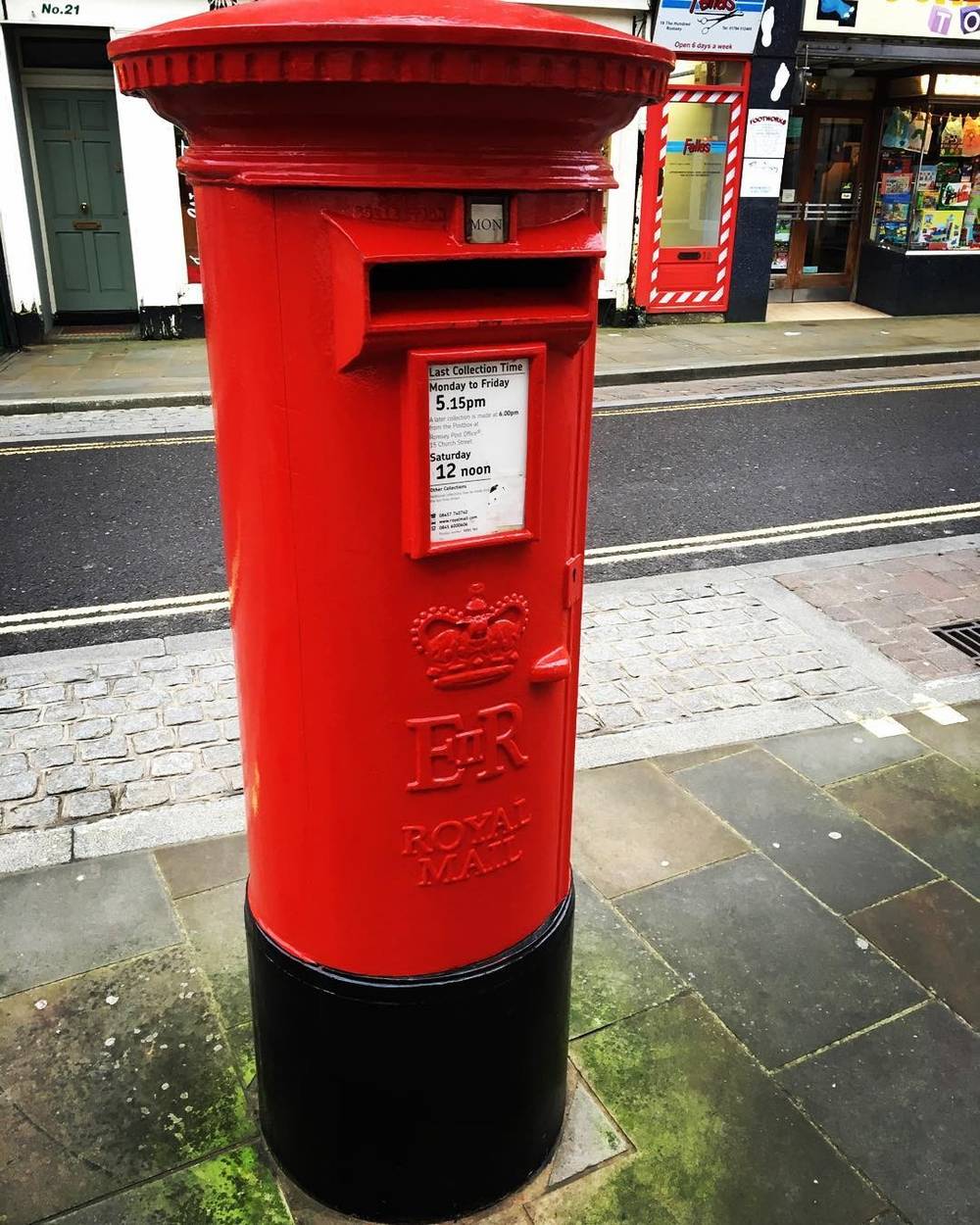 A traditional red Royal Mail post box on a UK street.